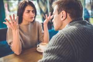 Frustrated woman gesticulates with her hands over coffee with a man