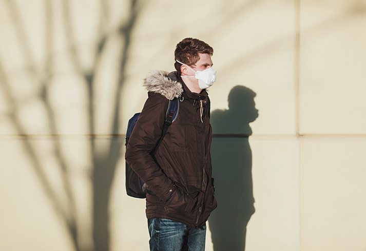 Male student with backpack and mask standing out in the cold.