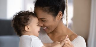 Smiling young African American mother hugging little infant
