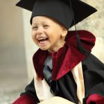 little boy dressed as a graduate with a book